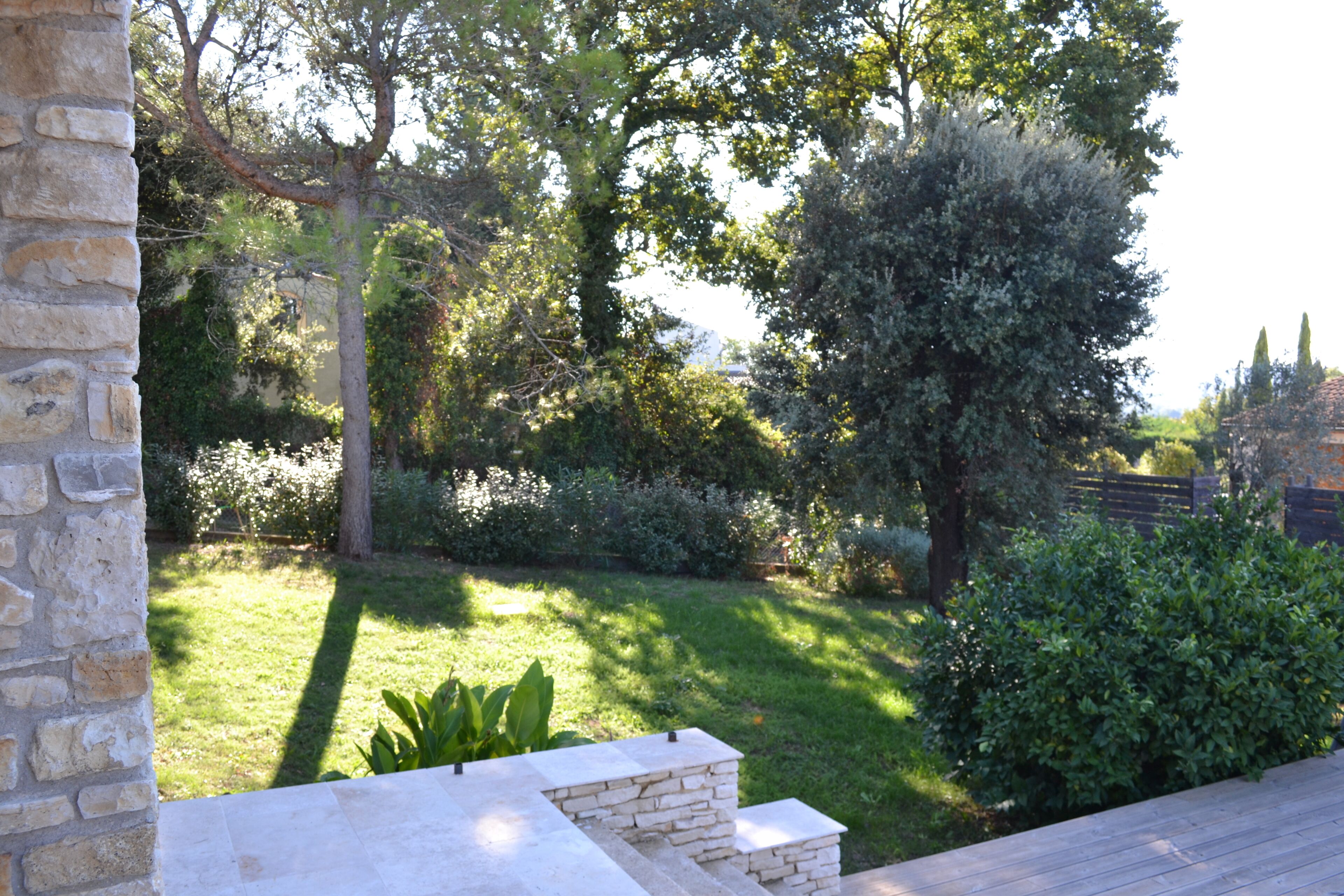 A stone wall, a wooden deck, and a well-maintained garden with various plants and trees.