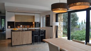 A modern kitchen with a central island, black chairs, and a dining table with a view of the outdoors. - Small house near Uzes and the Pont du Gard, ideal for 2 or 4 people (Saint-Maximin)