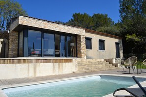 Una casa moderna amb piscina, façana de pedra, grans finestres i mobles d'exterior.