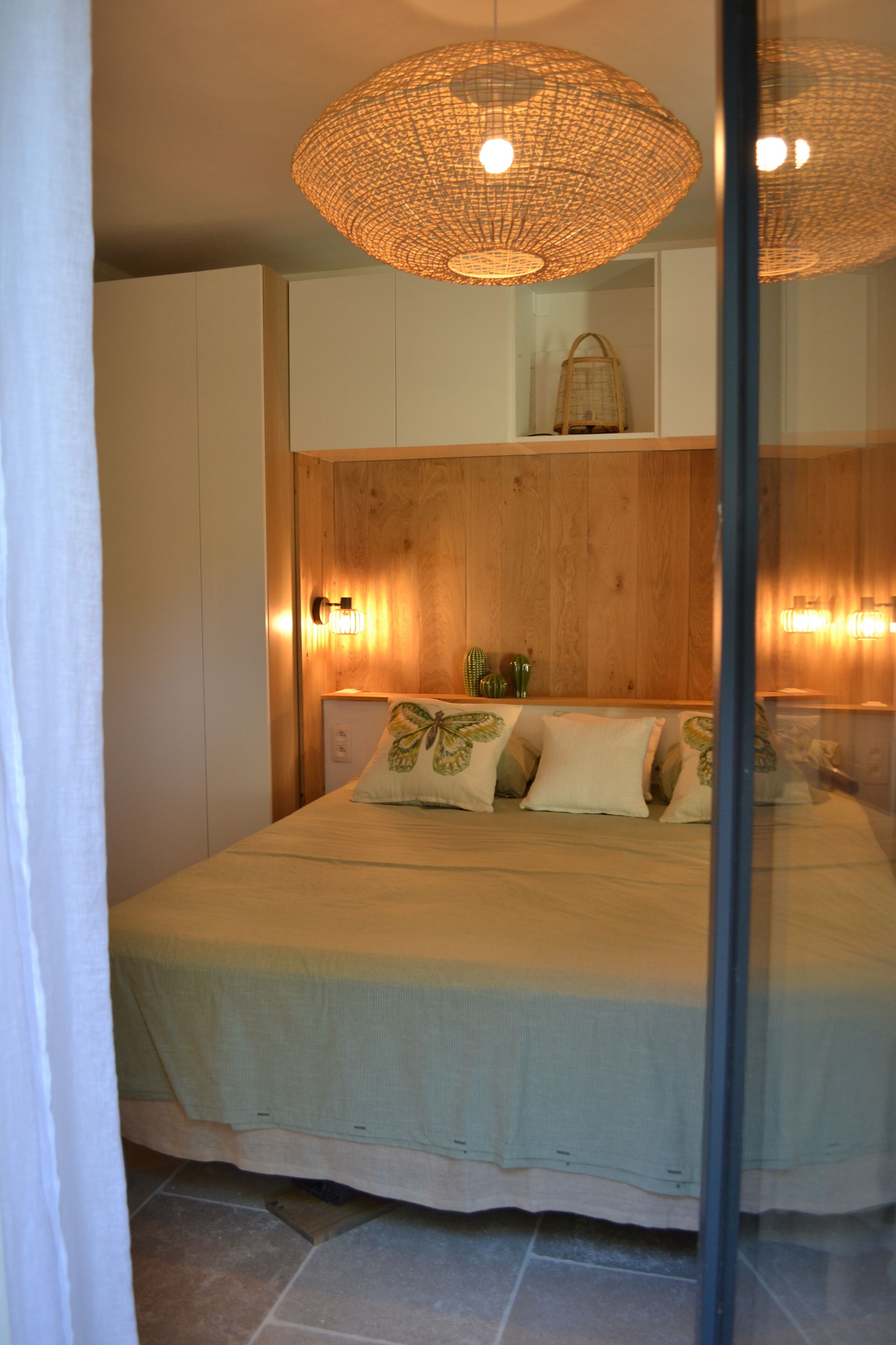 Un dormitorio con cama, lámparas de noche, cabecera de madera y una lámpara colgante.