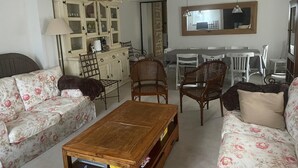 Un soggiorno con divano, tavolino, poltrone in vimini, un mobile con vetrine e un'area pranzo con tavolo e sedie.