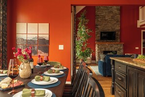 Un coin repas avec une table dressée pour six personnes, une cheminée en pierre et un téléviseur fixé au mur.