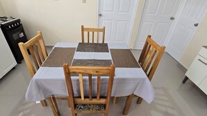 Un coin repas avec une table dressée pour quatre personnes, entourée de chaises en bois, d’un poêle et d’un petit meuble.