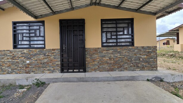 Un bâtiment doté d’une façade en pierre, d’une porte noire et de deux fenêtres ornées de grilles décoratives.