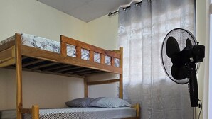 Une chambre avec un lit superposé, un ventilateur sur pied et un luminaire au plafond.