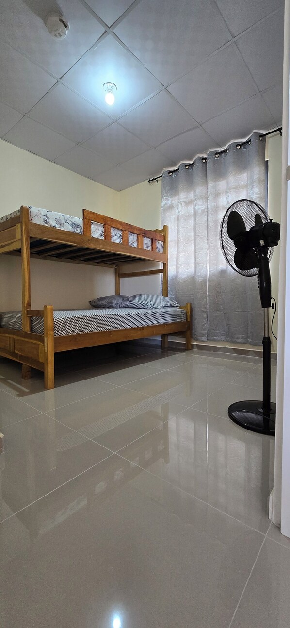 A room with a bunk bed, a standing fan, and a ceiling light.