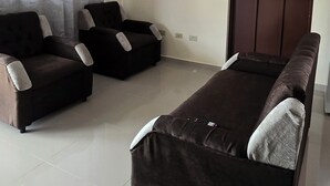 Une pièce comprenant un canapé, un lit, un luminaire au plafond, une porte et une fenêtre avec des rideaux.
