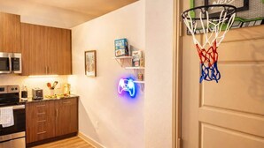 A kitchen with wooden cabinets, a microwave, and a neon game controller sign. - Cozy Designer Suite | Gym & Pool | DART Access (Irving)