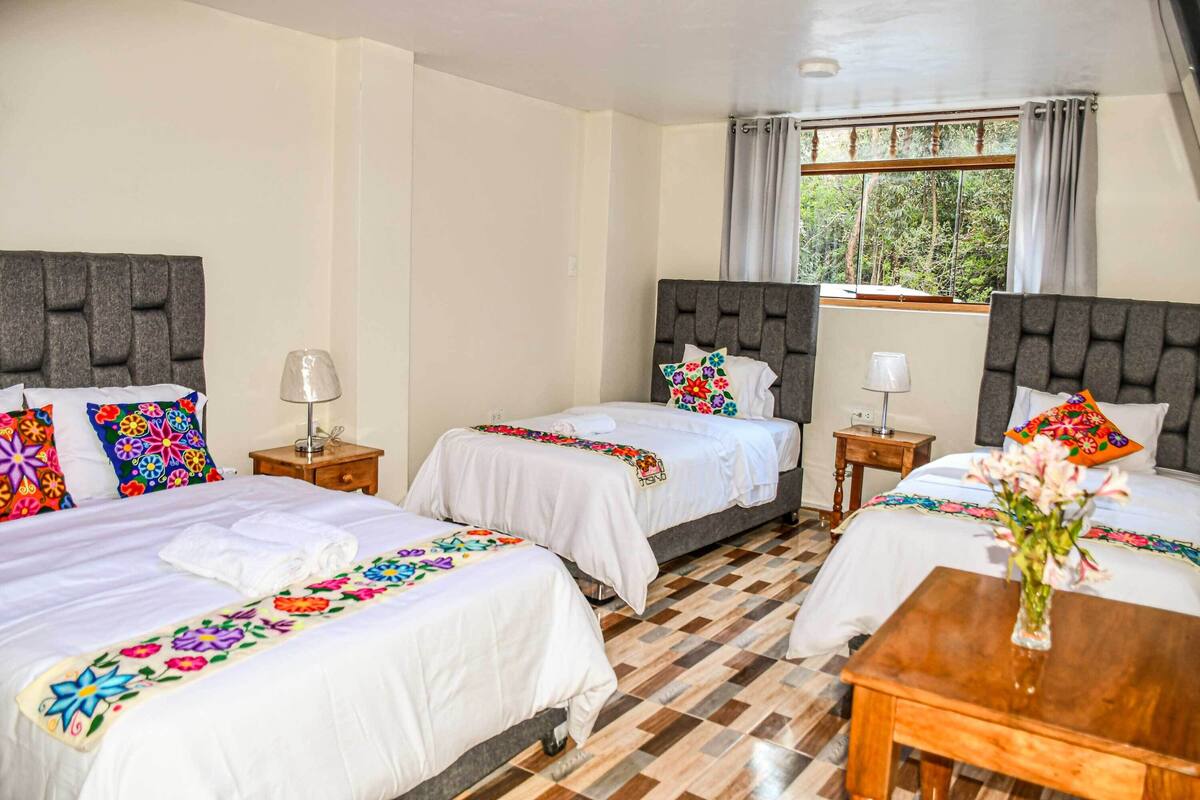 Une chambre d’hôtel avec deux lits, une table de chevet en bois, une petite table et une fenêtre avec des rideaux.
