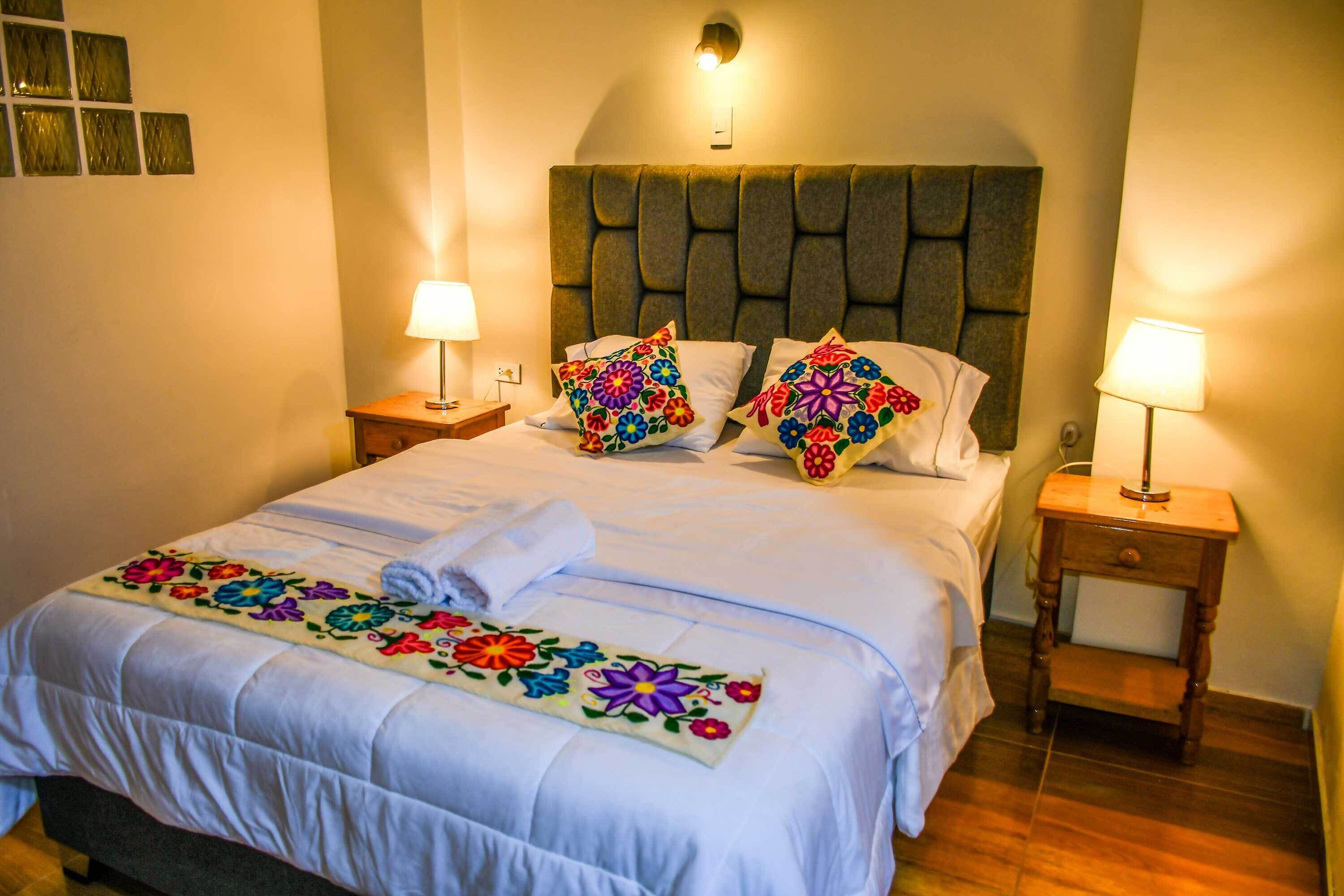A hotel room with a bed, two bedside tables, a headboard, and a decorative bedspread.
