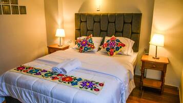 A hotel room with a bed, two bedside tables, a headboard, and a decorative bedspread.