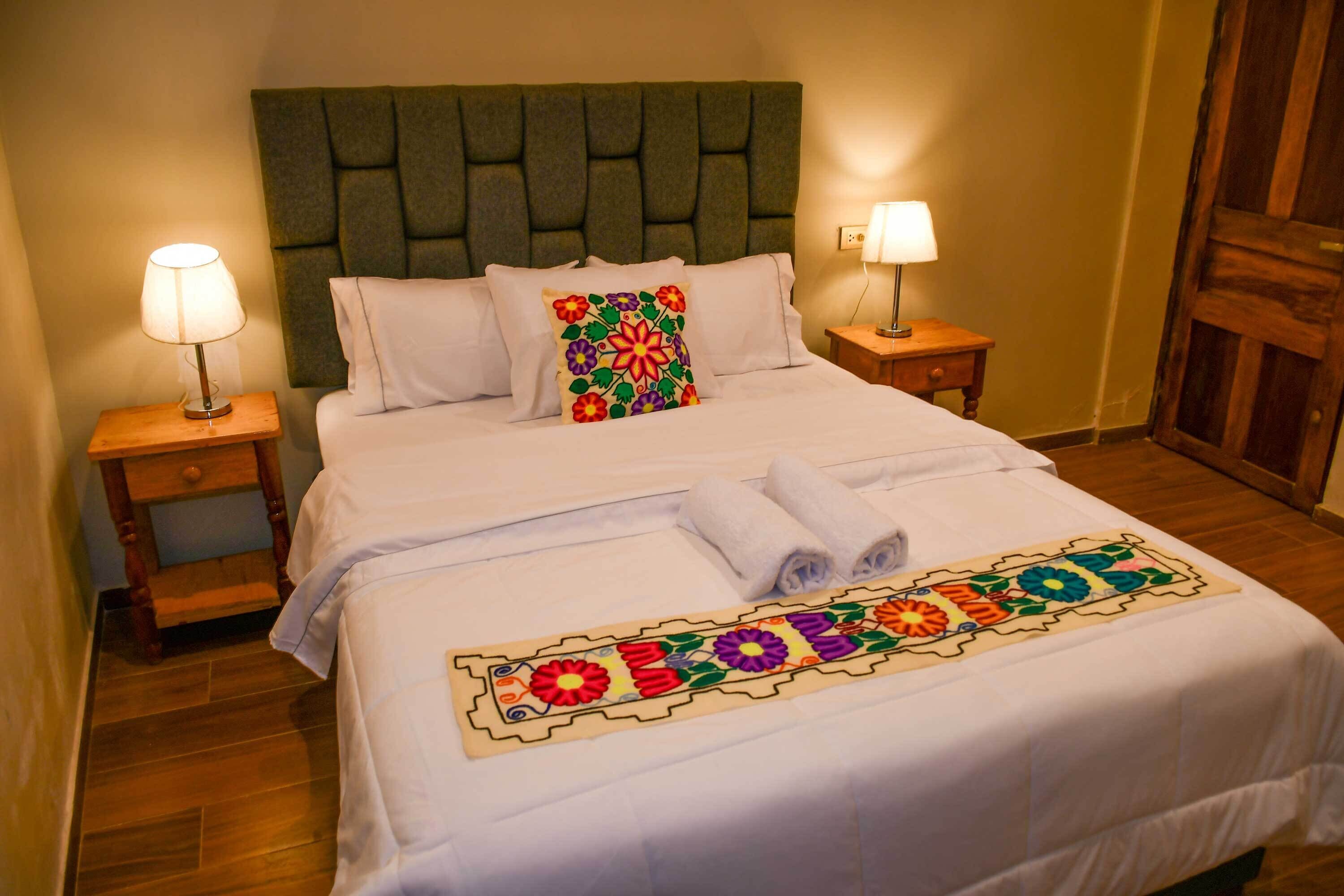 Una cama bien hecha con una colcha floral colorida, dos lámparas de noche y un cabecero de madera.
