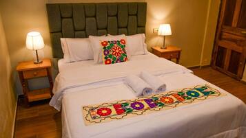 Una cama bien hecha con una colcha floral colorida, dos lámparas de noche y un cabecero de madera.