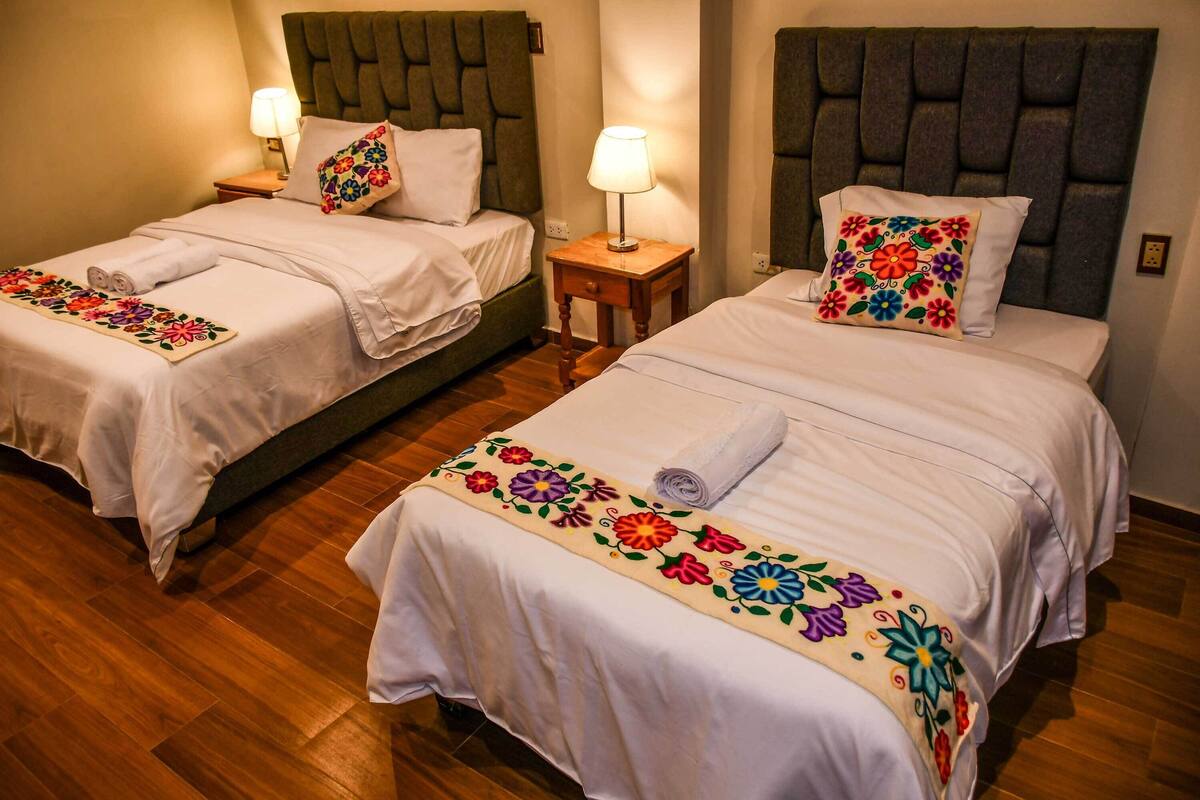 Deux lits jumeaux avec des têtes de lit, une table de chevet avec une lampe et une couvre-lit à motifs floraux.
