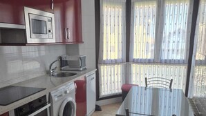 Eine kompakte Küche mit Mikrowelle, Backofen und Waschmaschine, ein Esstisch mit Stühlen sowie ein Blick durch ein blickdichtes Fenster.
