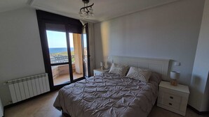 Ein Schlafzimmer mit einem großen Bett, einem Nachttisch, einer Lampe und Meerblick durch eine Schiebetür.