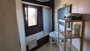 Ein kleines Badezimmer mit einer Badewanne, einem Waschbecken, einem Fenster und einem Ablagefach mit Toilettenartikeln.