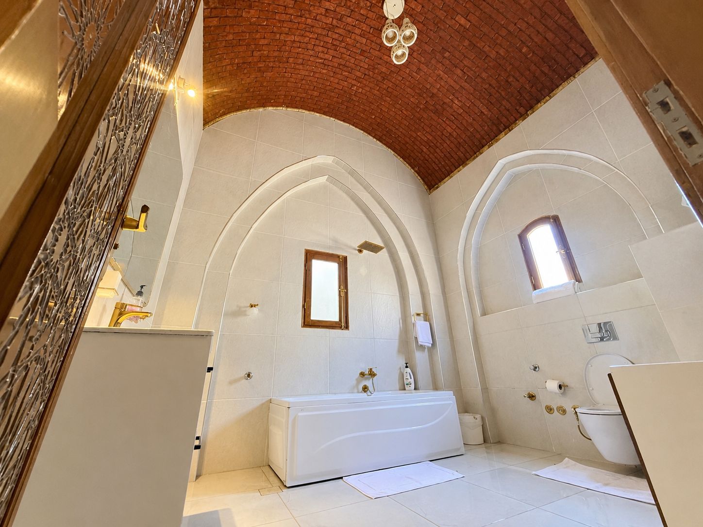 A bathroom with a white bathtub, a shower, and a toilet. There are arched ceilings and a brick wall.