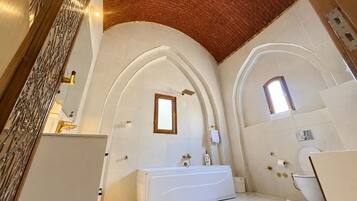 A bathroom with a white bathtub, a shower, and a toilet. There are arched ceilings and a brick wall.