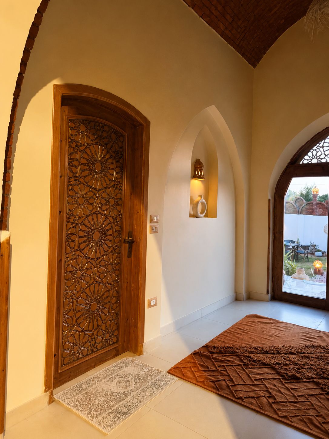 A room with a wooden door, a rug, and a small wall-mounted light fixture.