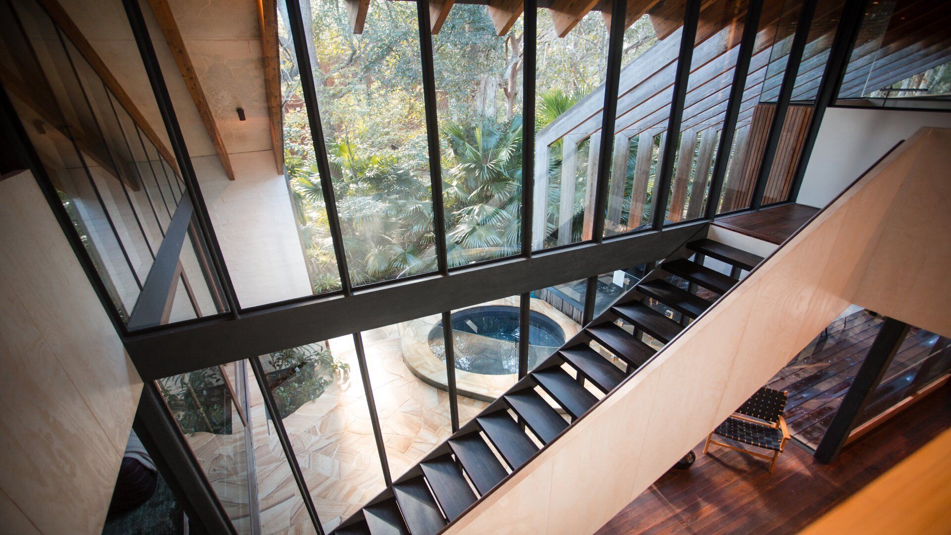 Un intérieur moderne avec une balustrade en verre, un escalier en bois et une vue sur un jardin extérieur.