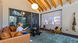 A modern living room with a large screen displaying a movie selection, leather furniture, and a rustic wall decor piece.
