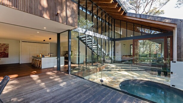 Ein modernes Haus mit einer verglasten Terrasse, einem Pool und einer Treppe, die zu einer oberen Ebene führt.