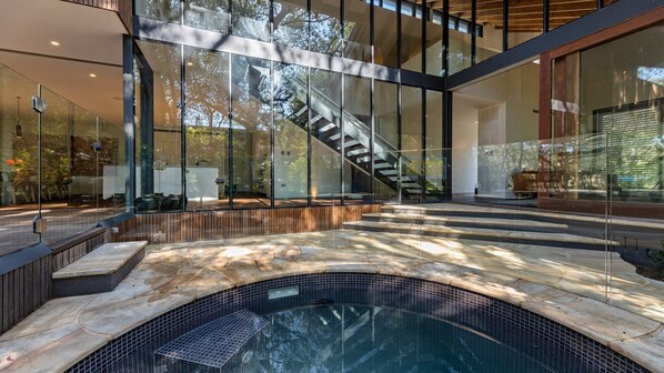 A modern interior with a glass staircase, a pool area, and a view of the outdoors.