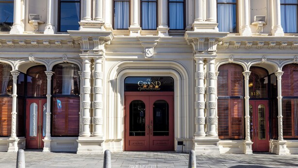 A grand building with a red entrance door, columns, and a sign reading 'The Grand Opera House.'