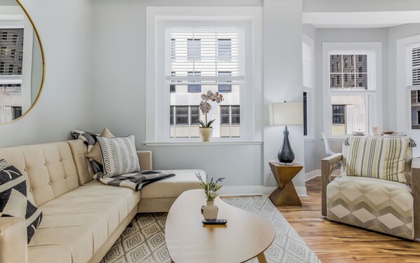 A living room with a sofa, armchair, coffee table, and a potted plant.