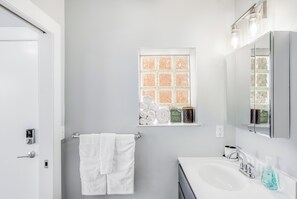 A bathroom with a white sink, a towel rack with two towels, a window with a view of the outside, and a mirror above the sink.