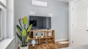 A modern bedroom with a television, wooden shelves, and a potted plant.