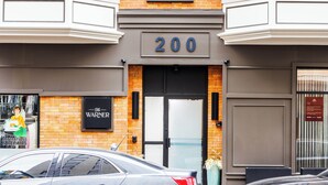 A building with a number '200' above the entrance, a sign for 'Warner,' and two cars parked in front.
