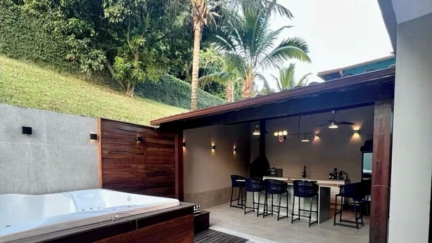 Ett modernt utomhusområde med en uppvärmd pool, en träveranda, en bar med barstolar och utsikt över palmer.
