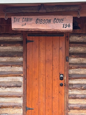 Een houten cabin-deur met een bord erboven met de tekst 'The Cabin at Gibson Cove 134'.