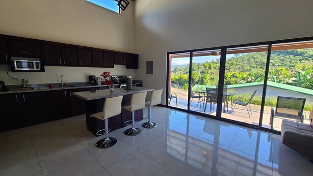 Una cocina moderna con una isla grande, taburetes de bar y vistas a exuberante vegetación a través de amplios ventanales.