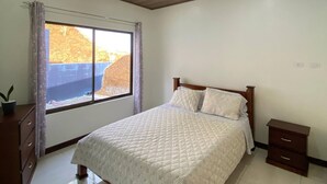 Un dormitorio con cama, ventana, techo de madera y piso de baldosas.