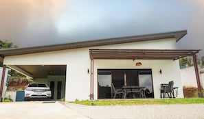 A modern two-story house with a garage, a covered patio area with outdoor furniture, and a car parked in the driveway. - Entire New House Hosted by Arelis (San Isidro)