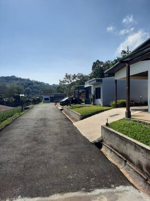 A modern building with a paved driveway, a covered walkway, and a view of a hilly landscape. - Entire New House Hosted by Arelis (San Isidro)