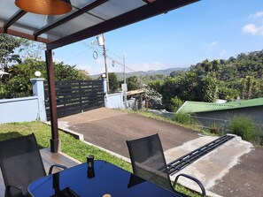 A patio with a table and chairs, a view of a green landscape, and a gated entrance. - Entire New House Hosted by Arelis (San Isidro)
