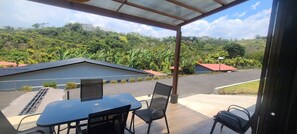 A covered outdoor area with a table and chairs, a view of a residential area with houses and lush greenery. - Entire New House Hosted by Arelis (San Isidro)