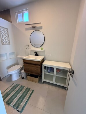 Une salle de bain comprenant des toilettes, un lavabo, un miroir, un meuble de rangement et une petite fenêtre.