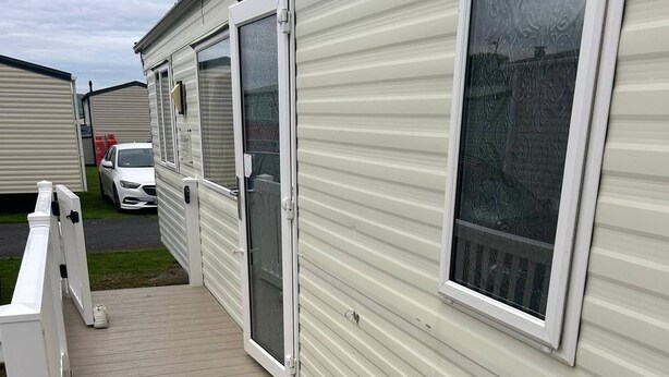 Una casa móvil con terraza de madera, puertas corredizas de vidrio y cerca blanca.