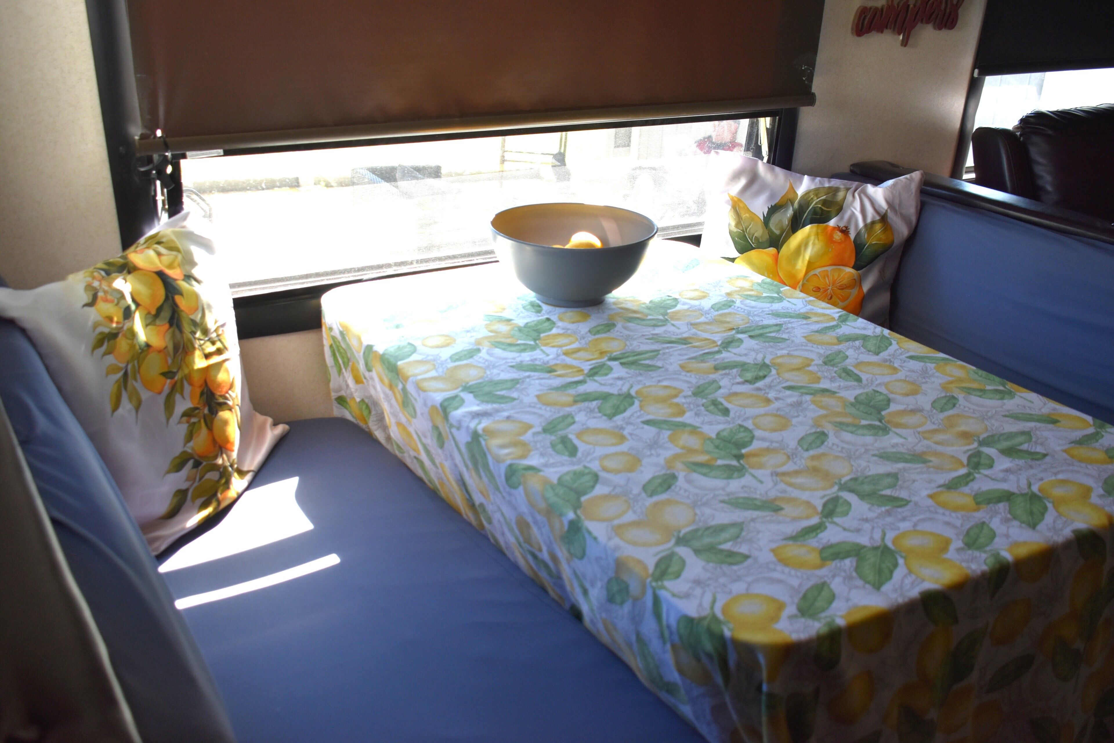 A small, compact room with a single bed, a table with a bowl on it, and a window with a view of the outside.