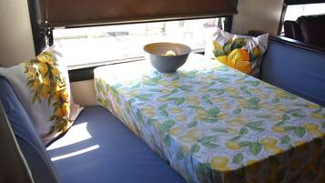 A small, compact room with a single bed, a table with a bowl on it, and a window with a view of the outside.