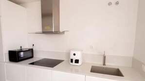 Cuina moderna amb armaris blancs, una campana extractora d'acer inoxidable, una placa d'inducció negra, una cafetera blanca i un rentaplat.