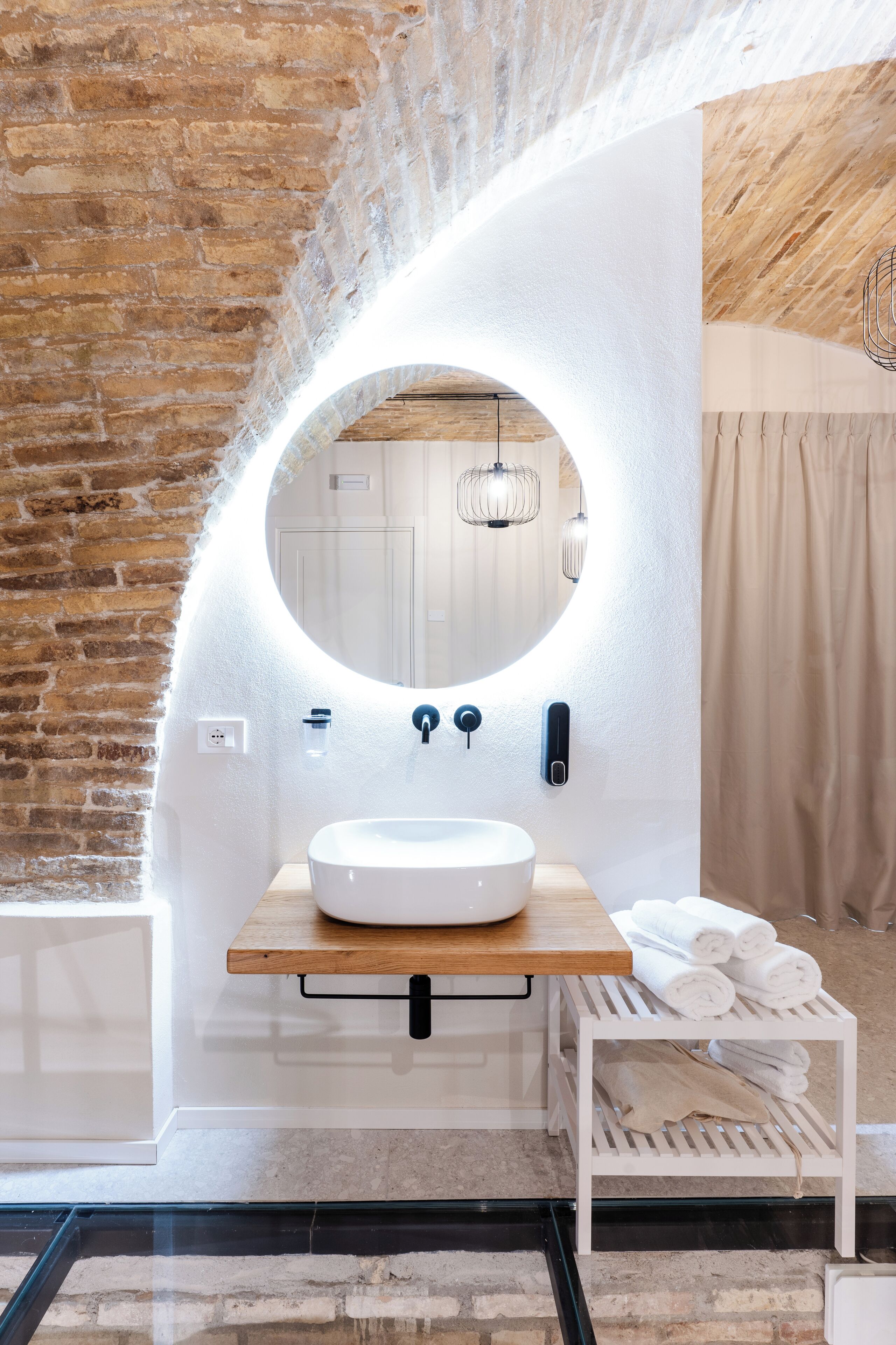 A bathroom with a round mirror, white sink, wooden countertop, and a towel rack.