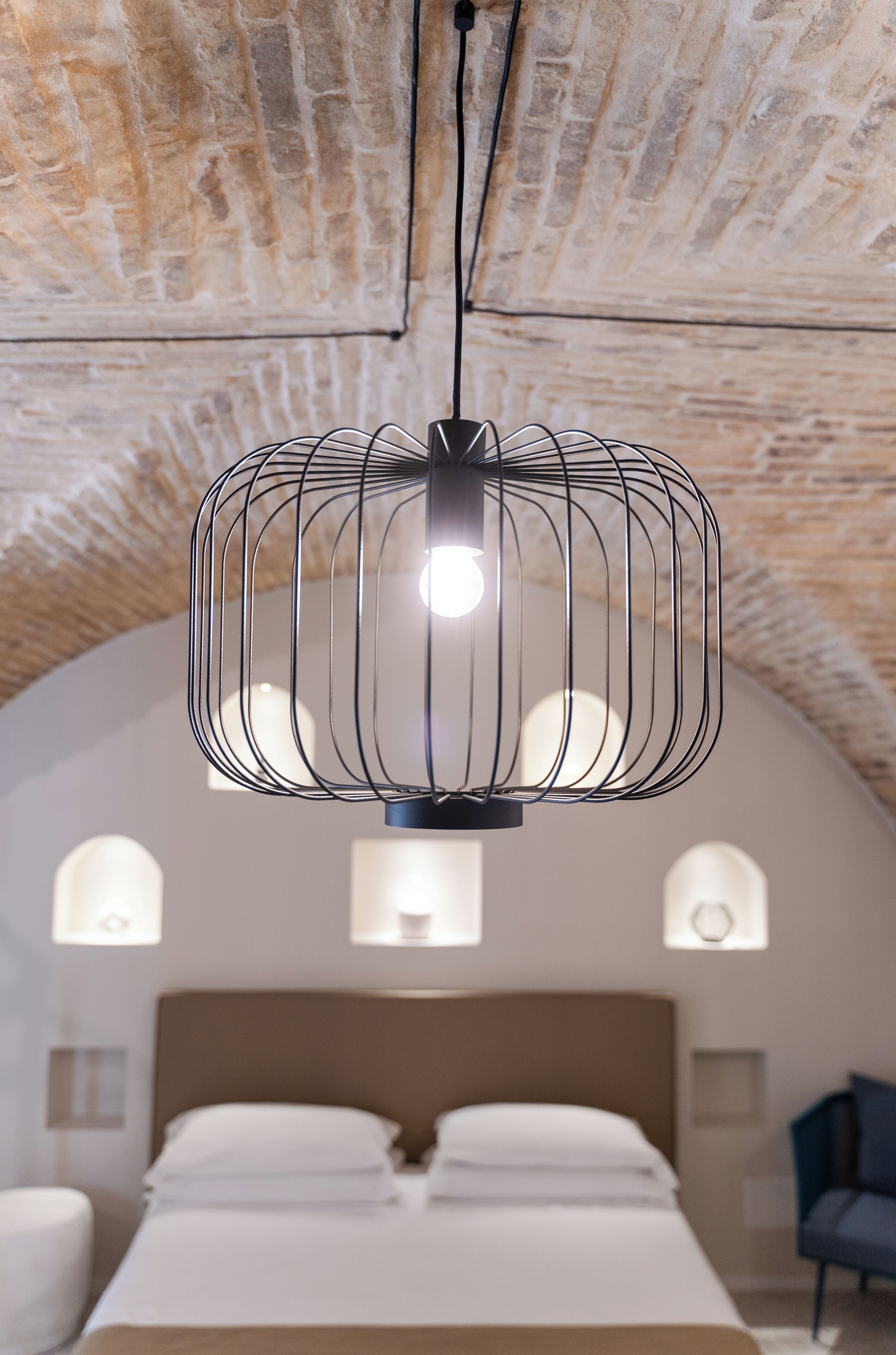 A modern bedroom with a unique curved ceiling, a bed with white linens, and a distinctive black wireframe pendant light.