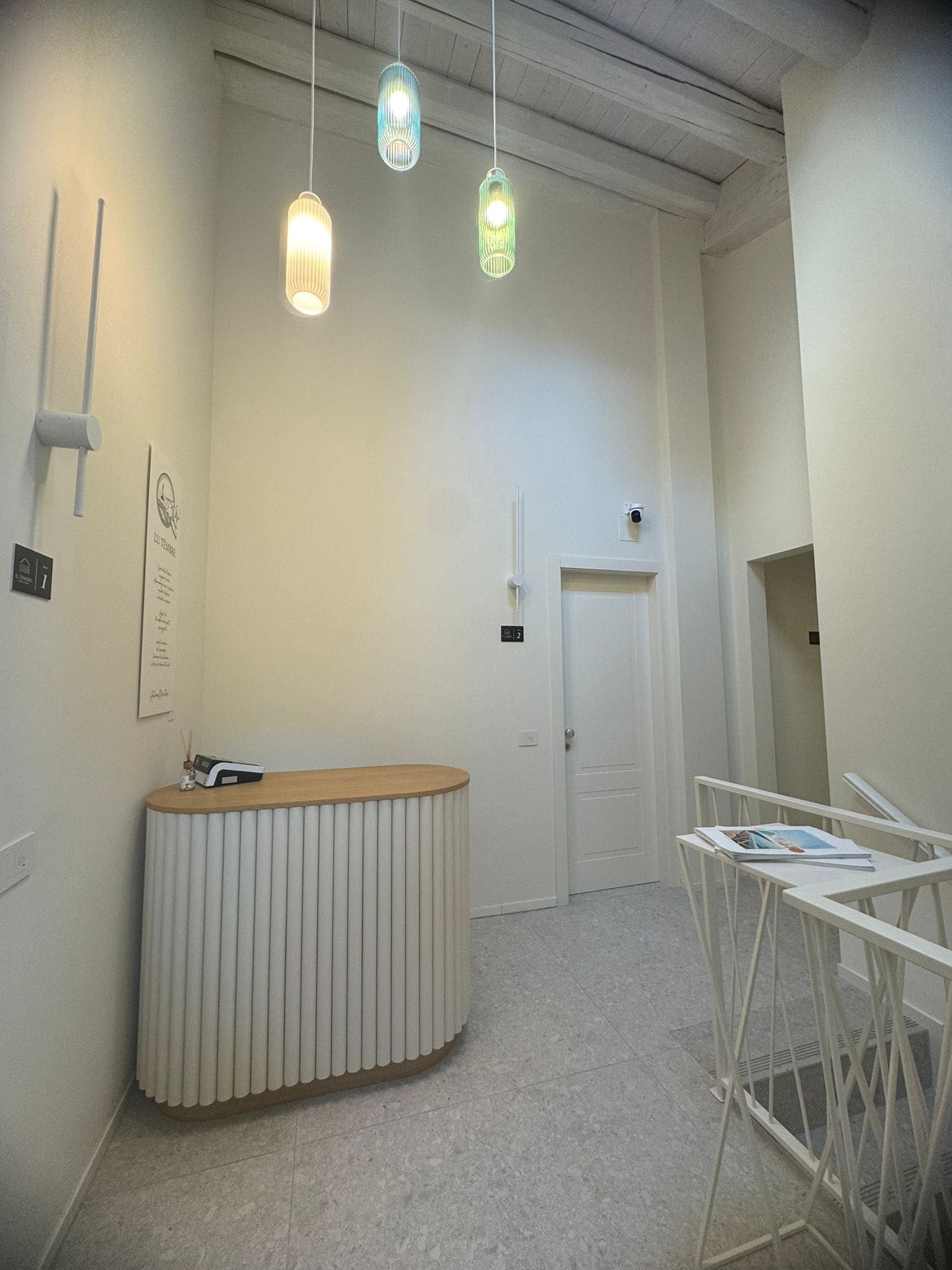 A reception desk with a white and wooden design, a white door, and hanging pendant lights.