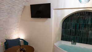 Ein modernes Badezimmer mit einer freistehenden Badewanne, einem an der Wand montierten Flachbildfernseher und einem kleinen runden Tisch mit einem Stuhl.